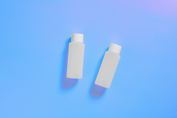 White cosmetic bottles on a blue neon background, bottle for cosmetic products, purple background