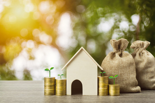 Saving money or property investment or buy a new home concept. A small house model with growth plant on stack of coins and money bag on wood table. Depicts sustainable financial goal.