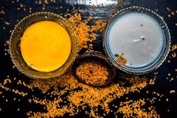 Curd or yogurt and oats face mask on the woodne surface in a glass bowl along with some raw oats in a black colored clay bowl and some spread on the surface. To Exfoliate Your Skin.