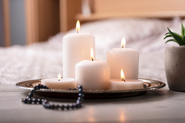 Composition of white burning candles on bedside table in light cozy bedroom interior. Selective focus.