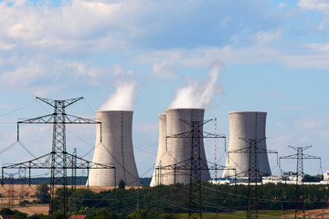 View of smoking chimneys of nuclear power plant, power lines and forest, under blue sky with clouds