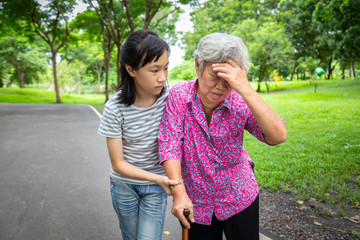 Asian senior grandmother has headache pain,touching her head with her hand,vertigo;dizziness;sick elderly people high blood pressure,feel faint,child girl or granddaughter care,help,support in outdoor