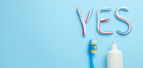 Word YES from toothpaste. Tube of colored toothpaste and  toothbrush on  blue background. The concept of proper cleaning and care of teeth. Copy space for text.