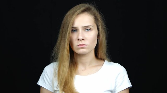 Portrait of unhappy caucasian woman looking at camera on black background. Upset young people and negative emotions concept.