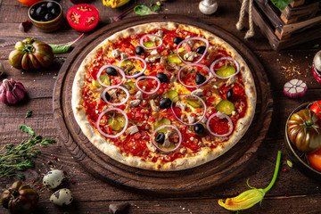 Tasty hot italian pizza Mexicana with Pork, Mozzarella, Pepperoni, Pickled Cucumbers, Olives, Tomatoes, Red Onions, Stewed Onions, Tomato Sauce  on old wooden table. Pizzeria menu. 
