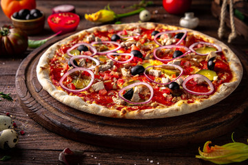 Tasty hot italian pizza Mexicana with Pork, Mozzarella, Pepperoni, Pickled Cucumbers, Olives, Tomatoes, Red Onions, Stewed Onions, Tomato Sauce  on old wooden table. Pizzeria menu. 