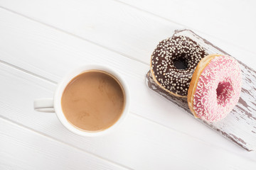 Pink and chocolate donuts with coffee with cream on white wooden table.