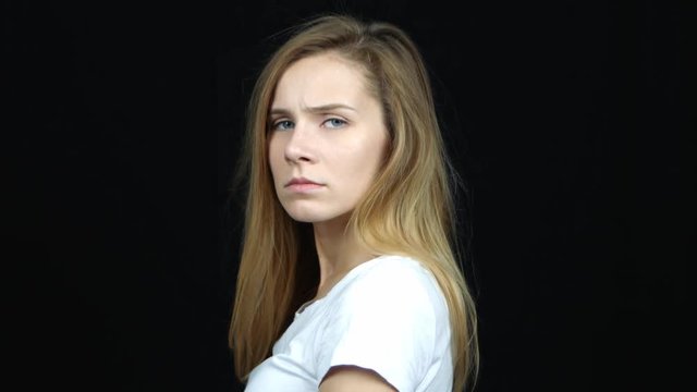Close up portrait of young handsome caucasian woman upset when turning to the camera. Sad female standing on black background.