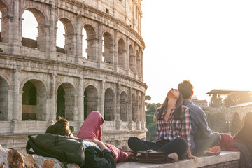 Three happy young friends sitting and lying in front of colosseum in rome
