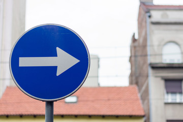 Right direction allowed one way blue street sign on a city street, against the gray buildings and...