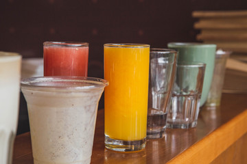 a red velvet cake on the background of glasses with various colored drinks (juice, coffee, smoothie, milkshake) standing on a white wooden table. A concept for a baker's dessert, a cafe, a restaurant