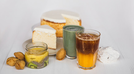 a big white cake  and piece of cake on plate on the background of glasses with drinks on a white wooden table. A concept for a baker's dessert, a cafe, a restaurant