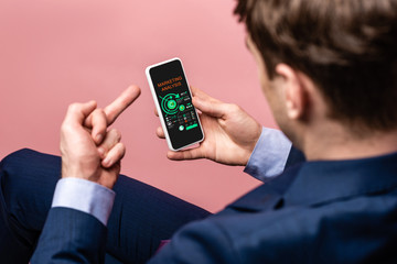 cropped view of businessman using smartphone with marketing analysis app while showing middle finger, isolated on pink