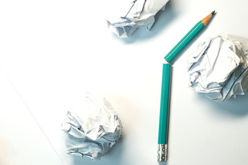 a broken green pencil on a white paper background nearby is three crumpled sheets of paper