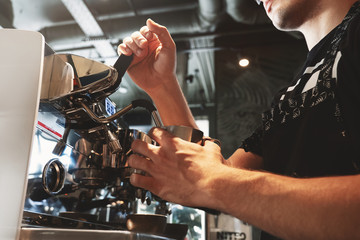 barista steaming milk in frothing pitcher using professional coffee machine cappuccinator in cafe