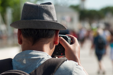 portrait on back view of photographer with hat taking a picture in the street