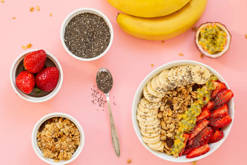 Smoothie bowl with Chia seeds, muesli, strawberries, banana slices and passion fruit on a pink background. Delicious and healthy Breakfast.