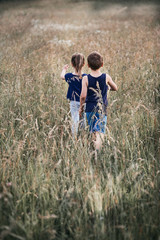 Little happy smiling kids playing in a tall grass in the countryside. Candid people, real moments, authentic situations