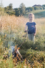 Little girl roasting marshmallow over a campfire on a meadow. Candid people, real moments, authentic situations