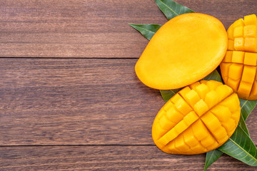 Fresh mango - beautiful chopped fruit with green leaves on dark wood background. Tropical fruit design concept. Flat lay. Top view. Copy space.