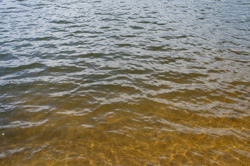 Waves on the lake with sandy bottom and reflection of the sun.