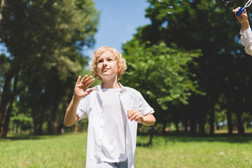 Fototapeta premium adorable boy in white Gesturing near soap bubbles in park