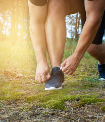 athlete in black uniform crouched and tying the laces on blue sneakers