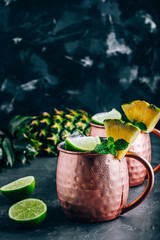Iced Cold Moscow Mule cocktail with lime and pineapple on dark background