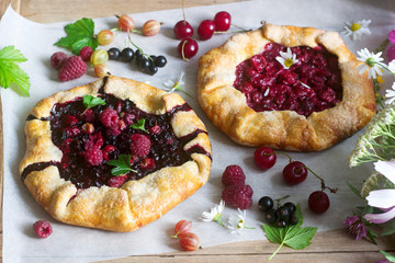 Galette pies with juicy berry filling, berries and wild flowers on a wooden background. Rustic style.