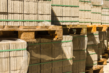 Plastersteine aus Beton auf Holzpaletten in Reihe und übereinander gestapelt, mit Zurrband gesichert und abgedeckt mit Plastikfolie als Regenschutz