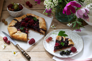 Sweet pie galette with juicy berry filling, berries and wild flowers on a wooden background. Rustic style.