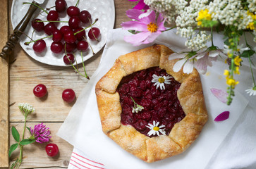 Sweet pie galette with juicy berry filling, berries and wild flowers on a wooden background. Rustic style.