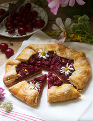 Sweet pie galette with juicy berry filling, berries and wild flowers on a wooden background. Rustic style.