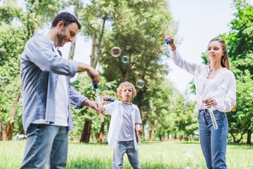 beautiful mother, father and son playing with soap bubbles in park