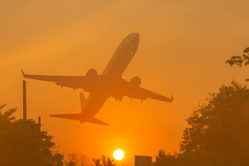 Silhouette comercial airplane flying on sunset over city.