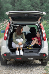 young mother with kid boy sitting in car trunk resting in summer sunny day