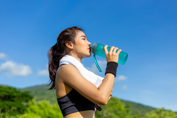 Beautiful young Asian woman exercising in the morning at a running track, taking a rest to drink water