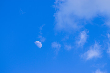 Half moon in the daytime sky with clouds.
