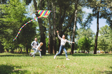 excited family running and playing with flying kite in park