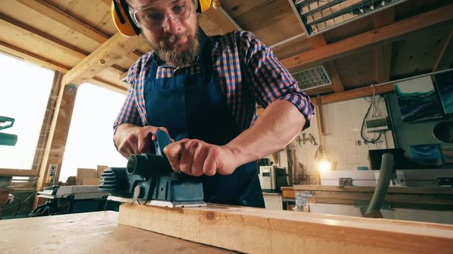 Male joiner uses a tool while working with wood. Carpenter working.