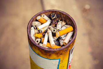 Ashtray at the smoking place, full of the variety of cigarettes after smoked. Dark toned, closed up
