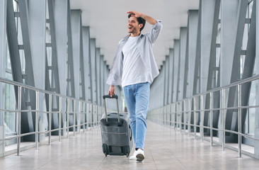 Fototapeta na wymiar Cheerful man walking with luggage at airport