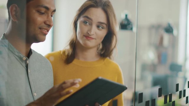 Portrait of Handsome Indian Man Showing Touch Screen Digital Tablet Computer To His Beautiful Female Team Member, They Discuss Project Details. Successful Young People Working in Diverse Office