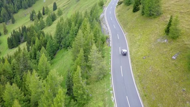Aerial, tilt up, drone shot, following a Jeep car, driving on a mountain road, at Grossglockner pass, on a cloudy summer day, in Heiligenblut, Austria