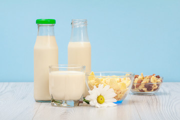 Two bottles and glass of milk, bowl with muesli on blue background.