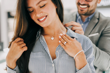 Middle age couple enjoying in shopping at modern jewelry store. Young woman try it out gorgeous...