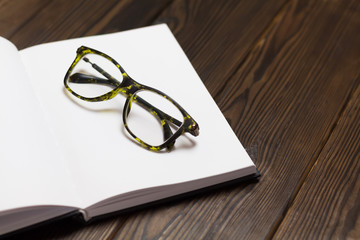 Open blank book, pen and glasses on dark wooden table. View from above. Space for text.