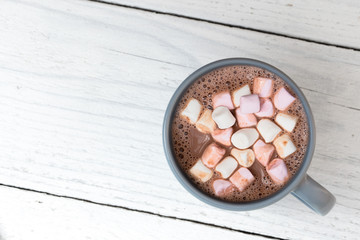 Hot chocolate with small marshmallows in a blue-grey ceramic mug isolated on white painted wood from above. Space for text.