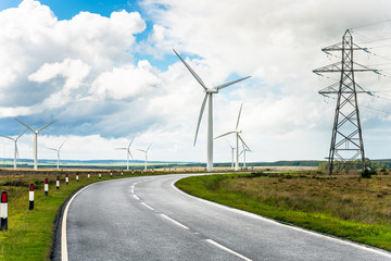 Fototapeta na wymiar Winding road running through wind turbines and high voltage pylons