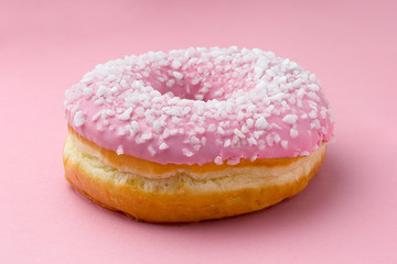 Pink frosted donut sprinkled with crystal sugar isolated on pink background.